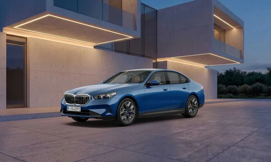 파이토닉 블루 메탈릭 색상의 BMW i5 xDrive40 M 스포츠 파이토닉 블루 에디션이 콘크리트 건물 앞에 좌측 앞 3/4 각도로 서 있는 모습. 20인치 바이컬러 블랙 그레이 휠과 어둡게 마감한 키드니 그릴이 보인다