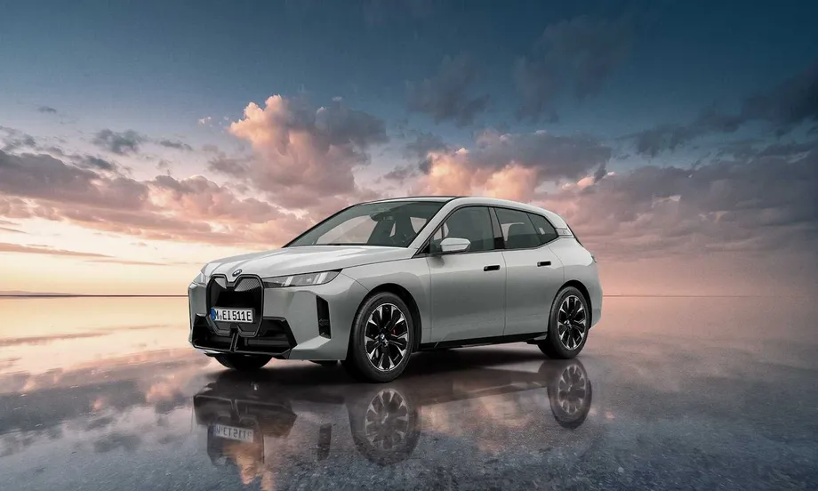 스페이스 실버 메탈릭 색상의 BMW iX xDrive45 M 스포츠 프로 스페이스 실버 에디션이 노을 진 평평한 수면 위에 좌측 앞 3/4 각도로 서 있는 모습. 21인치 에어로다이내믹 멀티컬러 휠과 빨간색 브레이크 캘리퍼가 보인다